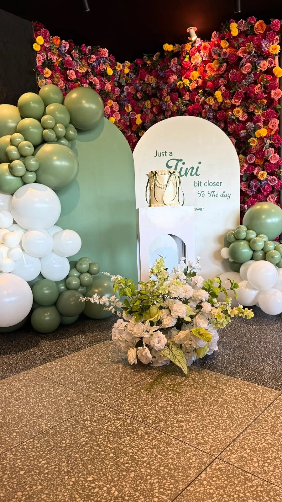 Bridal shower backdrop with sage and white balloons, a flower wall and a custom sign