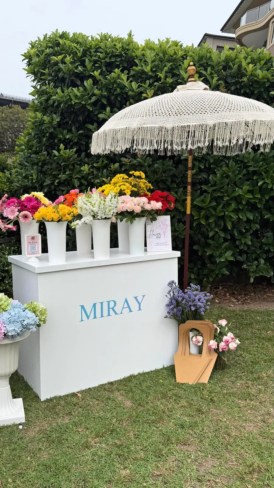 Flower bar with bright fresh flowers in white buckets under a fringed umbrella