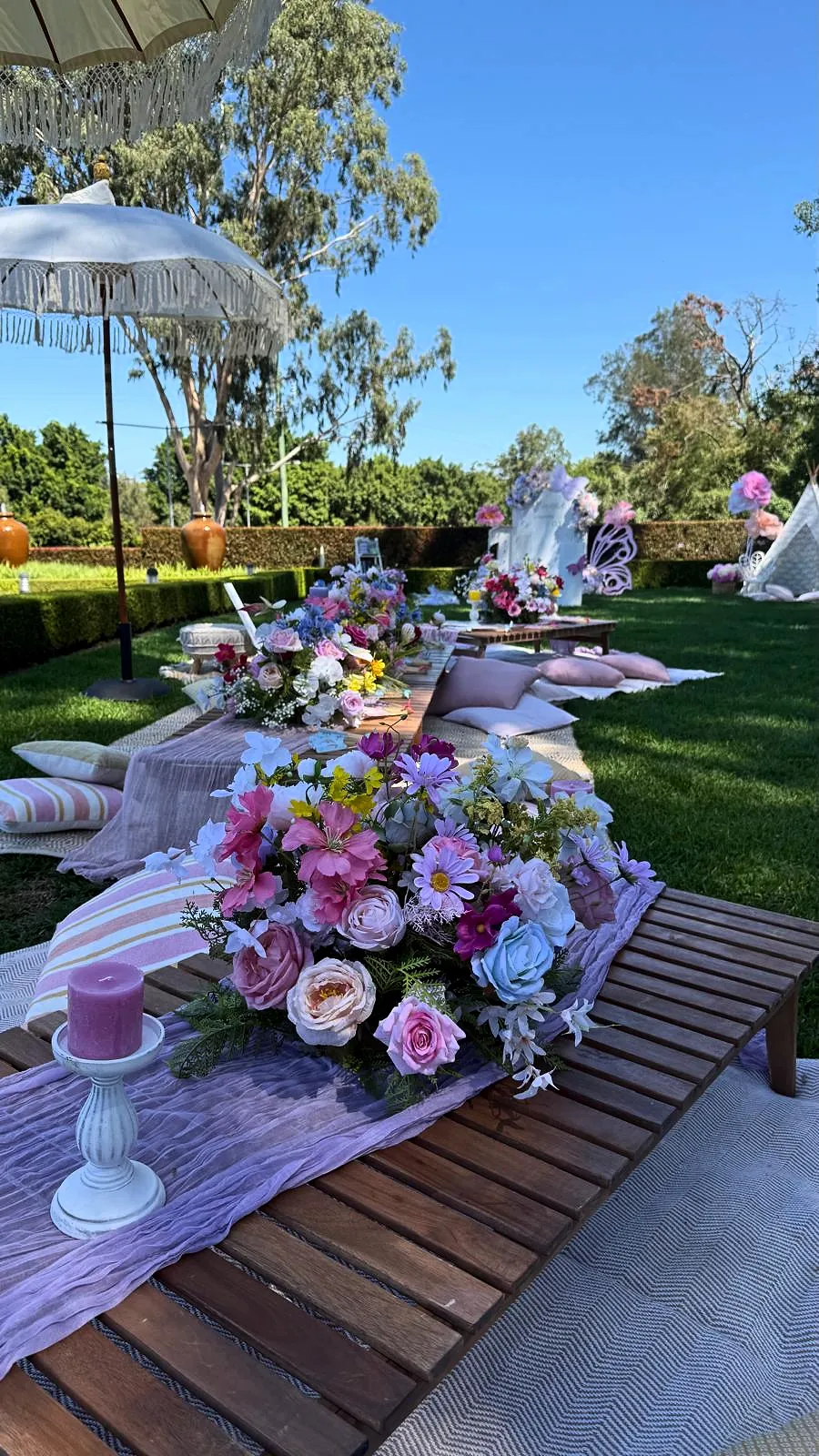 Long low table with pink and lilac florals and candles on a garden lawn