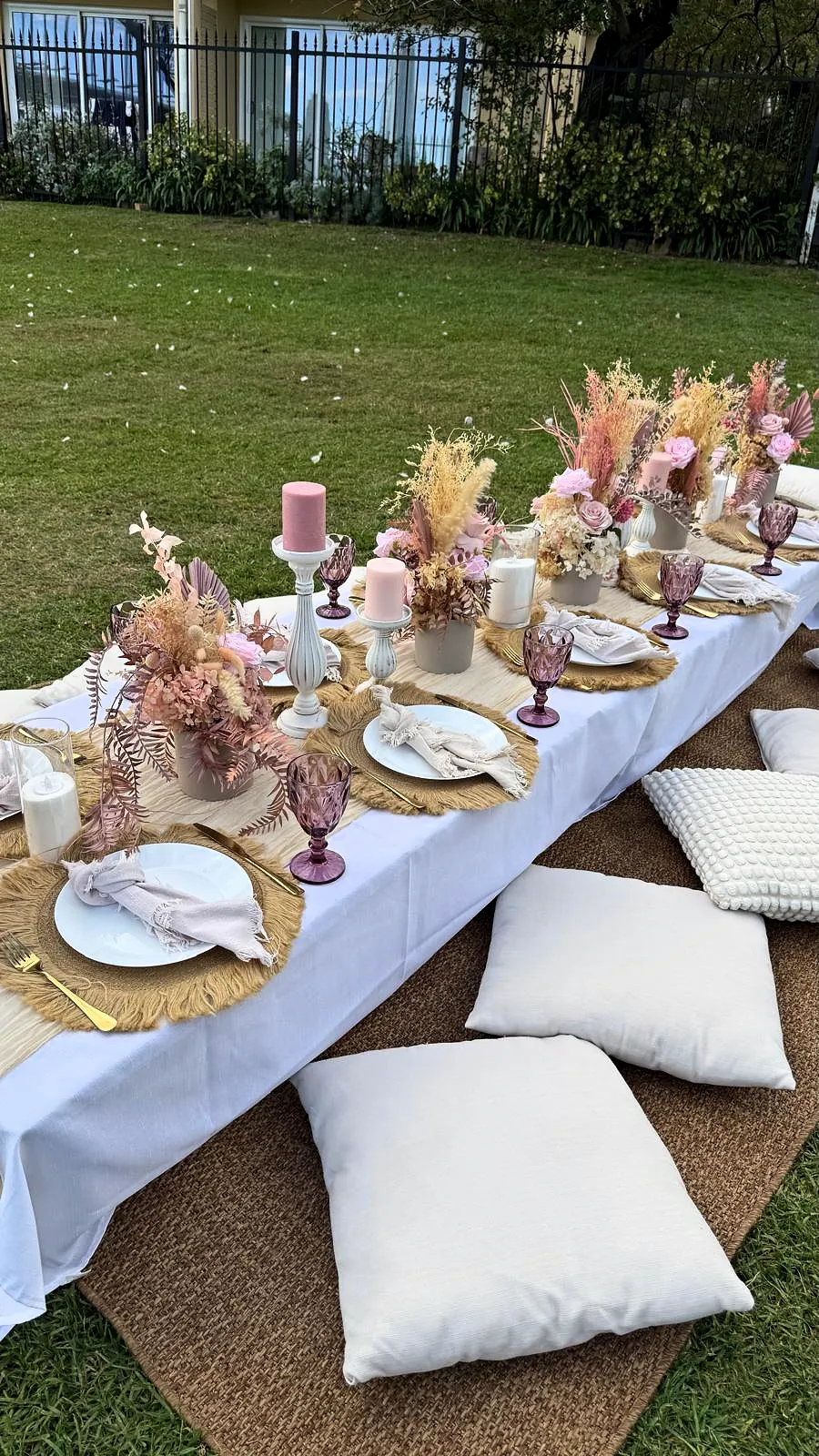 White picnic table with dried florals, candles and cushions on a sunny lawn