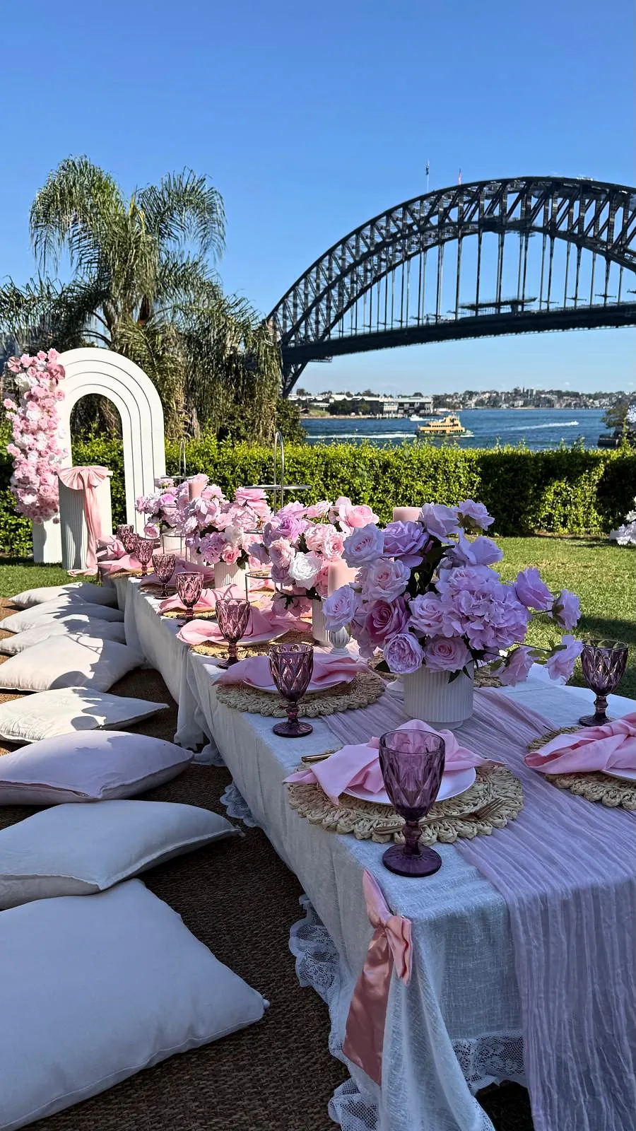 Pink picnic with a floral arch and low tables beside Sydney Harbour Bridge