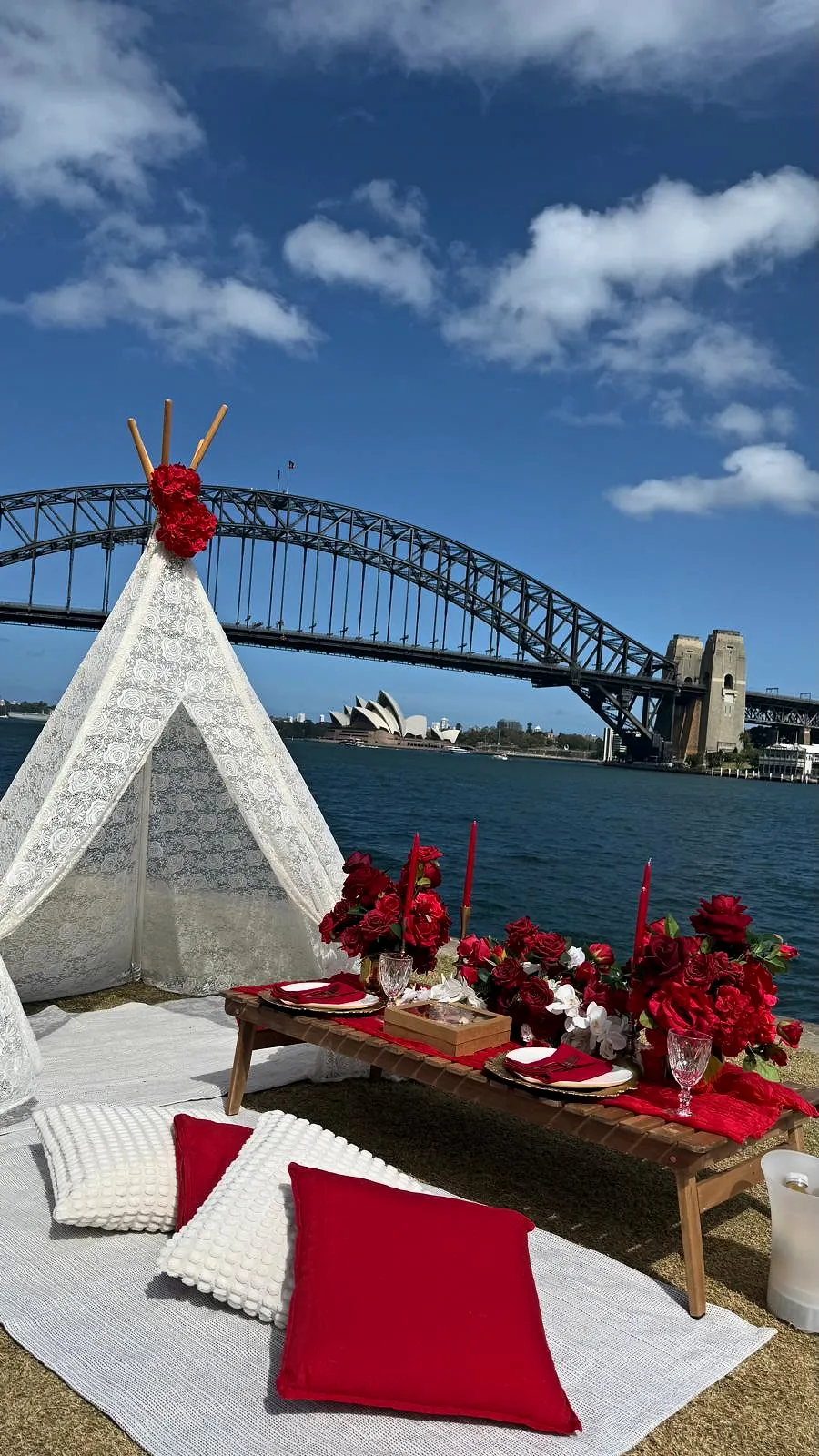 Lace teepee and low picnic table with red roses overlooking Sydney Harbour Bridge and the Opera House