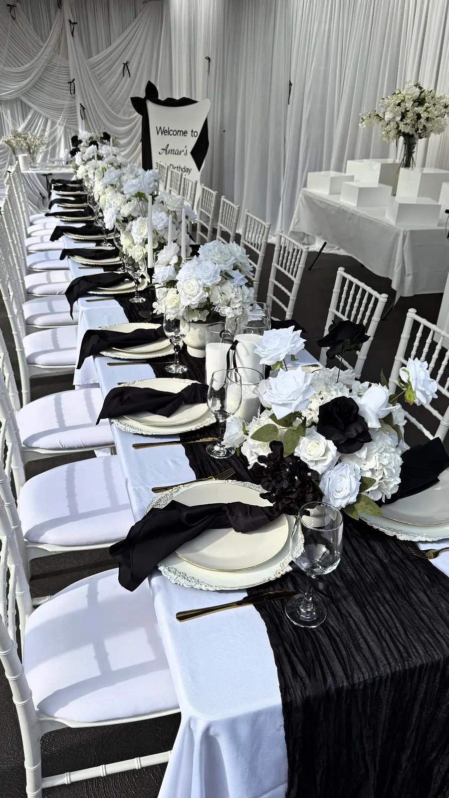Long table with black runners, white florals and black napkins in a white-draped room