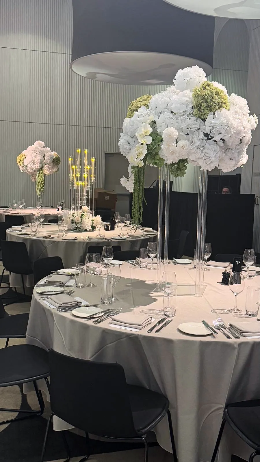 Reception tables with tall white hydrangea arrangements on glass stands and candelabras